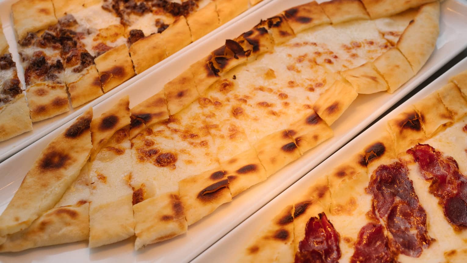 Three Turkish pide flatbreads on rectangular white plates