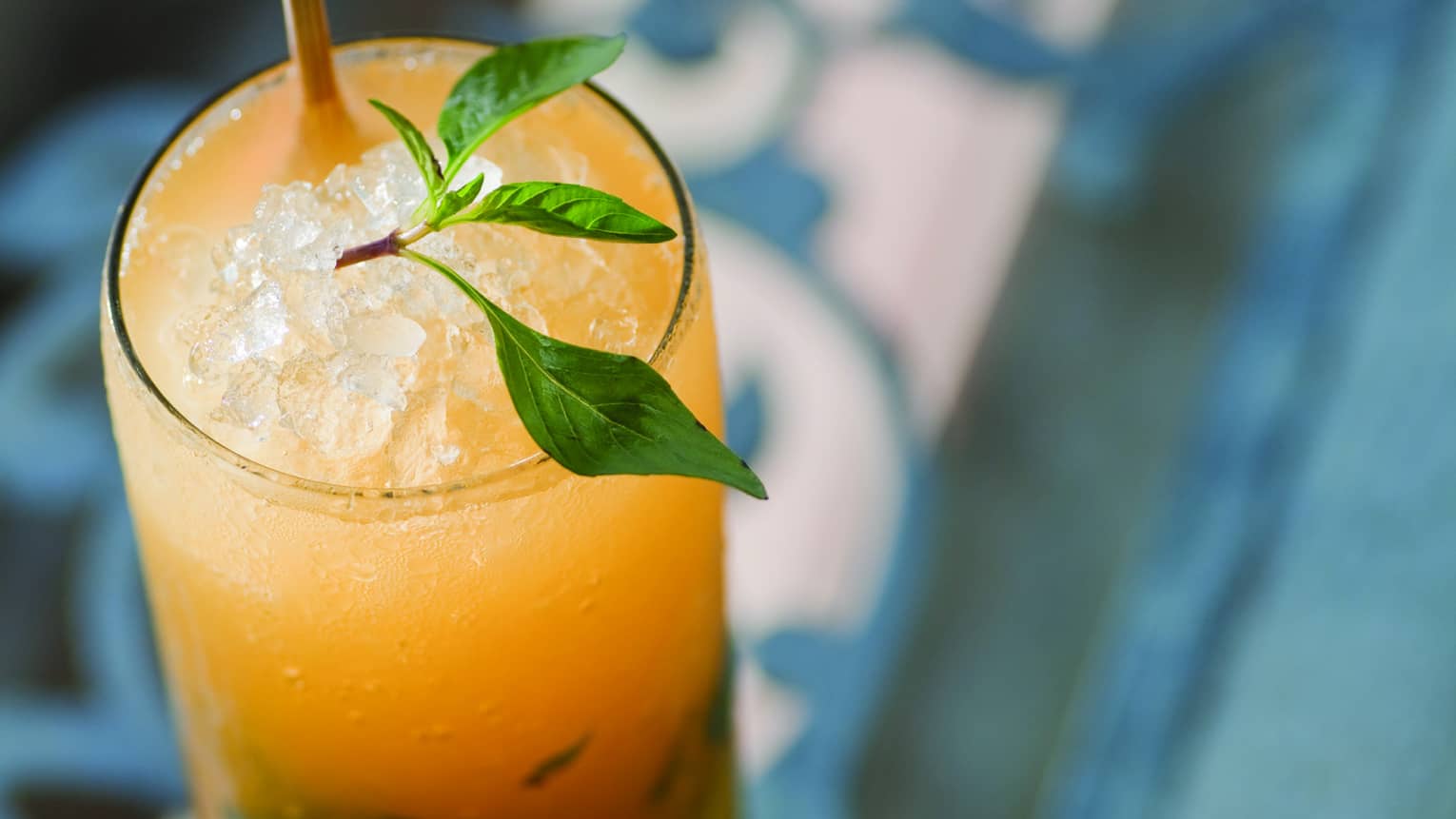 Bright yellow cocktail in tall glass with crushed ice, garnished with sprig of Thai basil