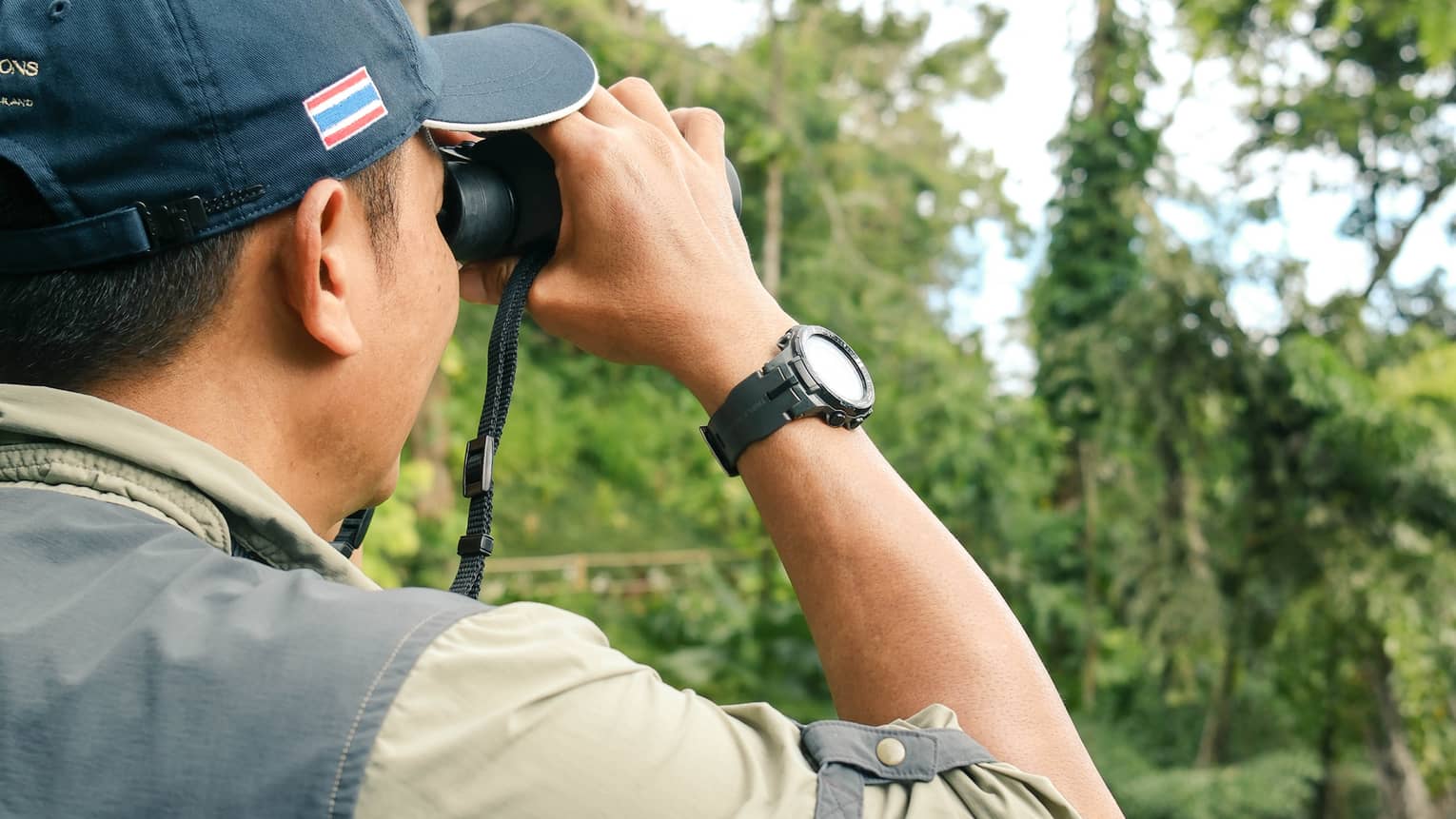 A man looks for birds through binoculars in jungle