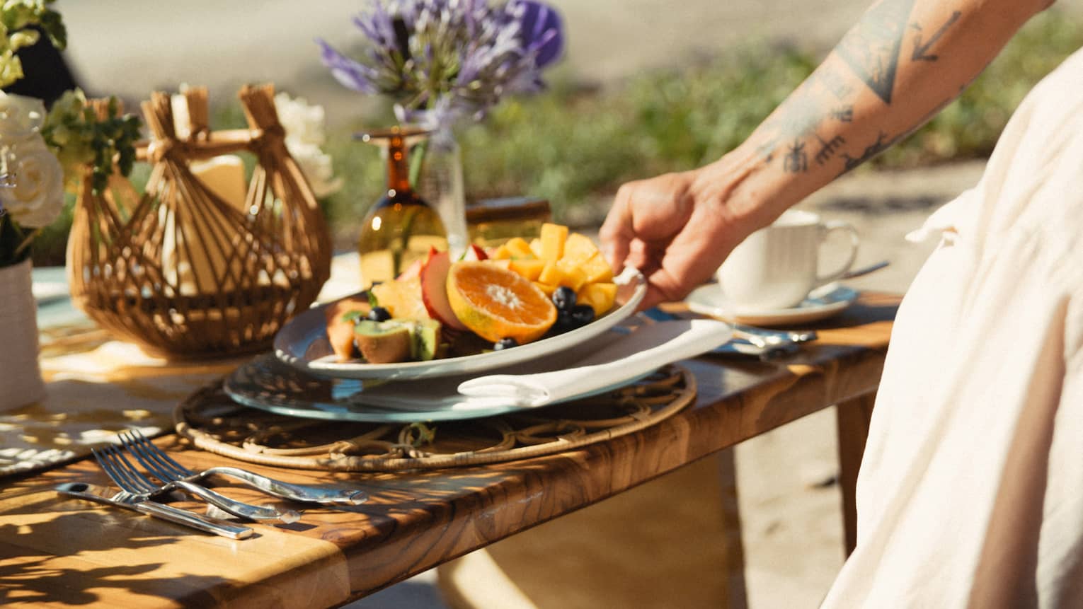 Server places a plate of brunch food down on an outdoor wooden table set on the beach
