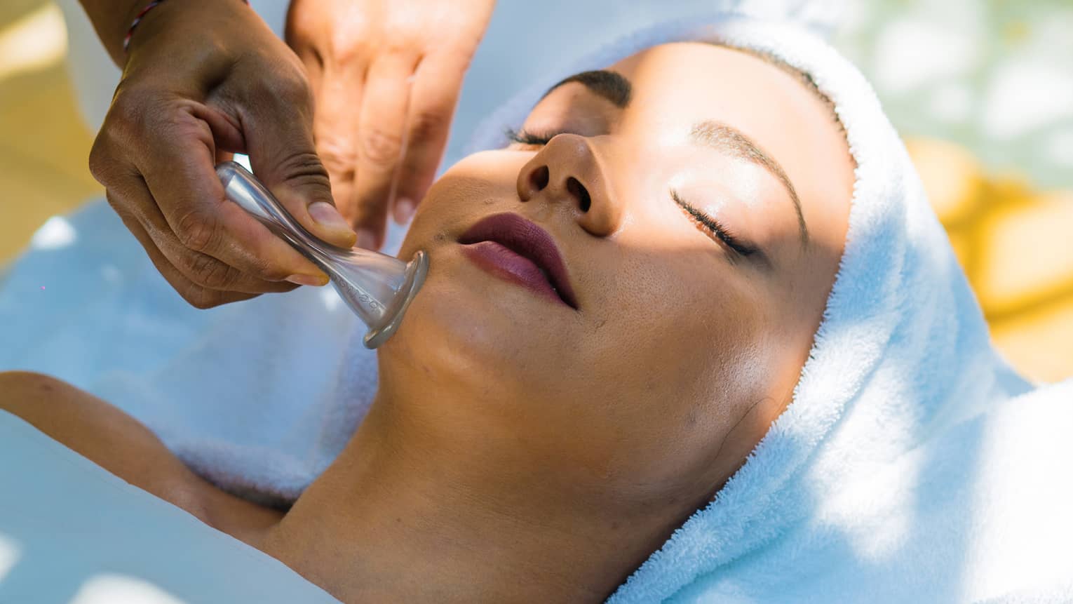 A woman lays on a table as a masseuse uses a roller on her face.