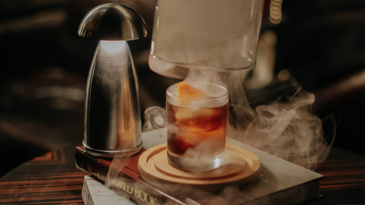 Aegri Somnia Signature Drink presented under a smoke cloche