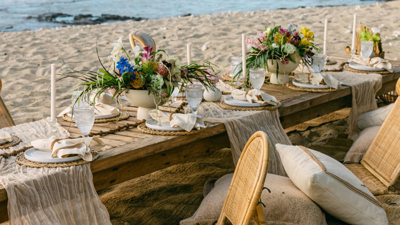 Low dining table set on the beach for an elaborate gourmet picnic, with floral arrangements and candle sticks