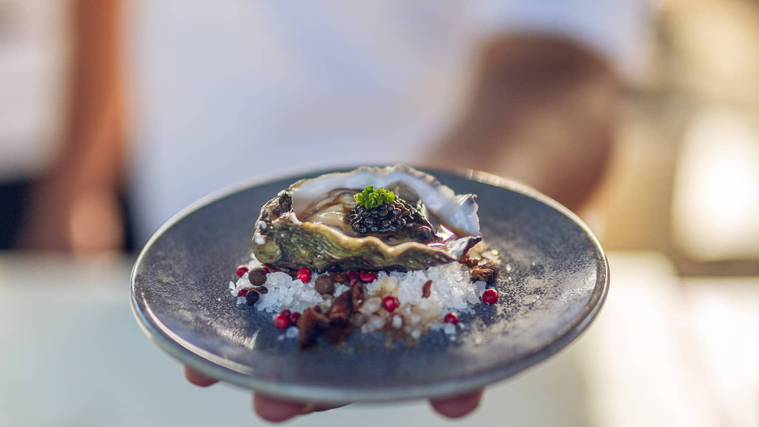 Chef holds a plate containing a fresh oyster