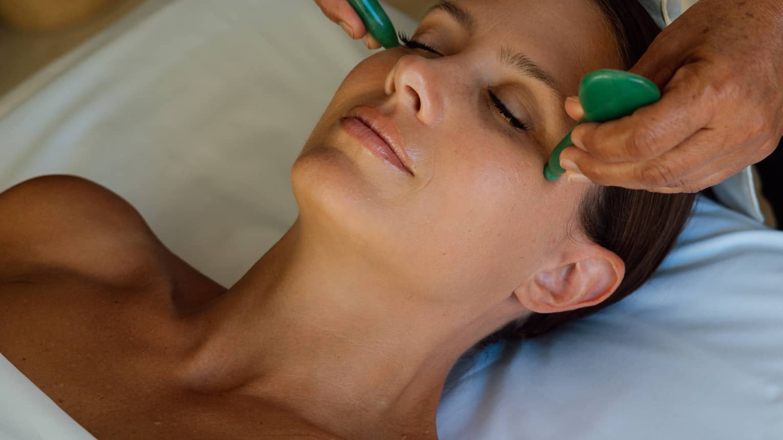 Guest getting a face massage while laying on a massage table.
