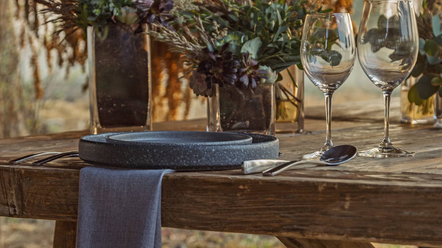 Outdoor wooden table set with plates and wine glasses