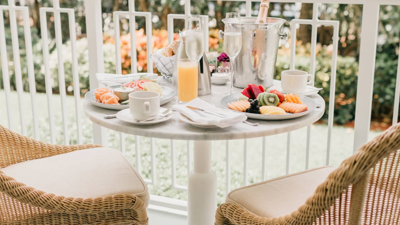 Balcony of a hotel room with two chairs and small round table, overlooking gardens