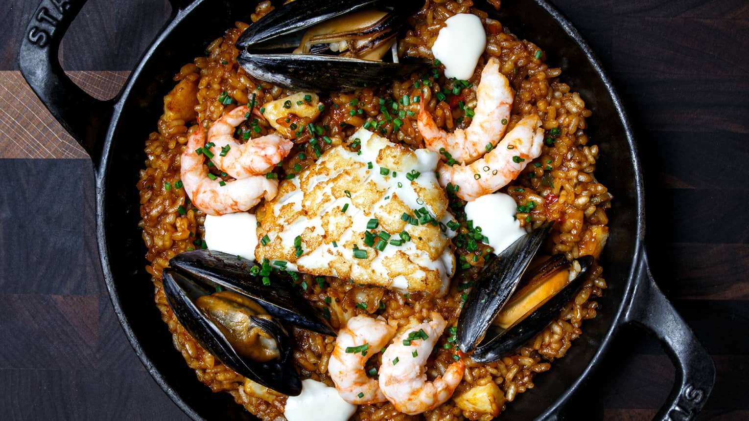 Prawns, squid and mussels on a bed of red Bomba rice in a black Staub brand cast iron skillet 