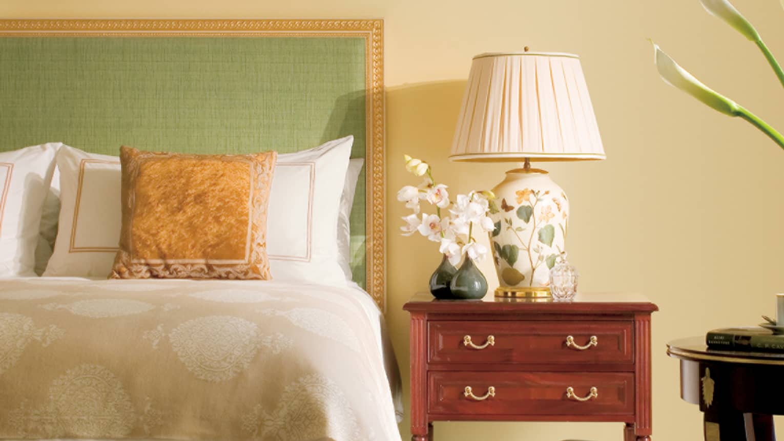 Close-up of Superior City-View Room bed with green headboard, gold frame and accent pillow, bedside lamp and orchid