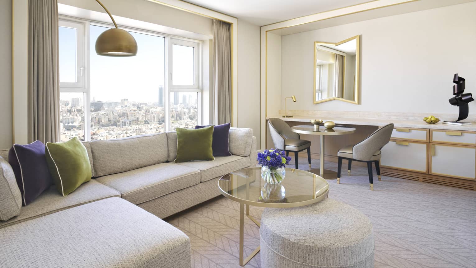 A cozy parlour room with an L-shaped couch, and a cityscape view. 