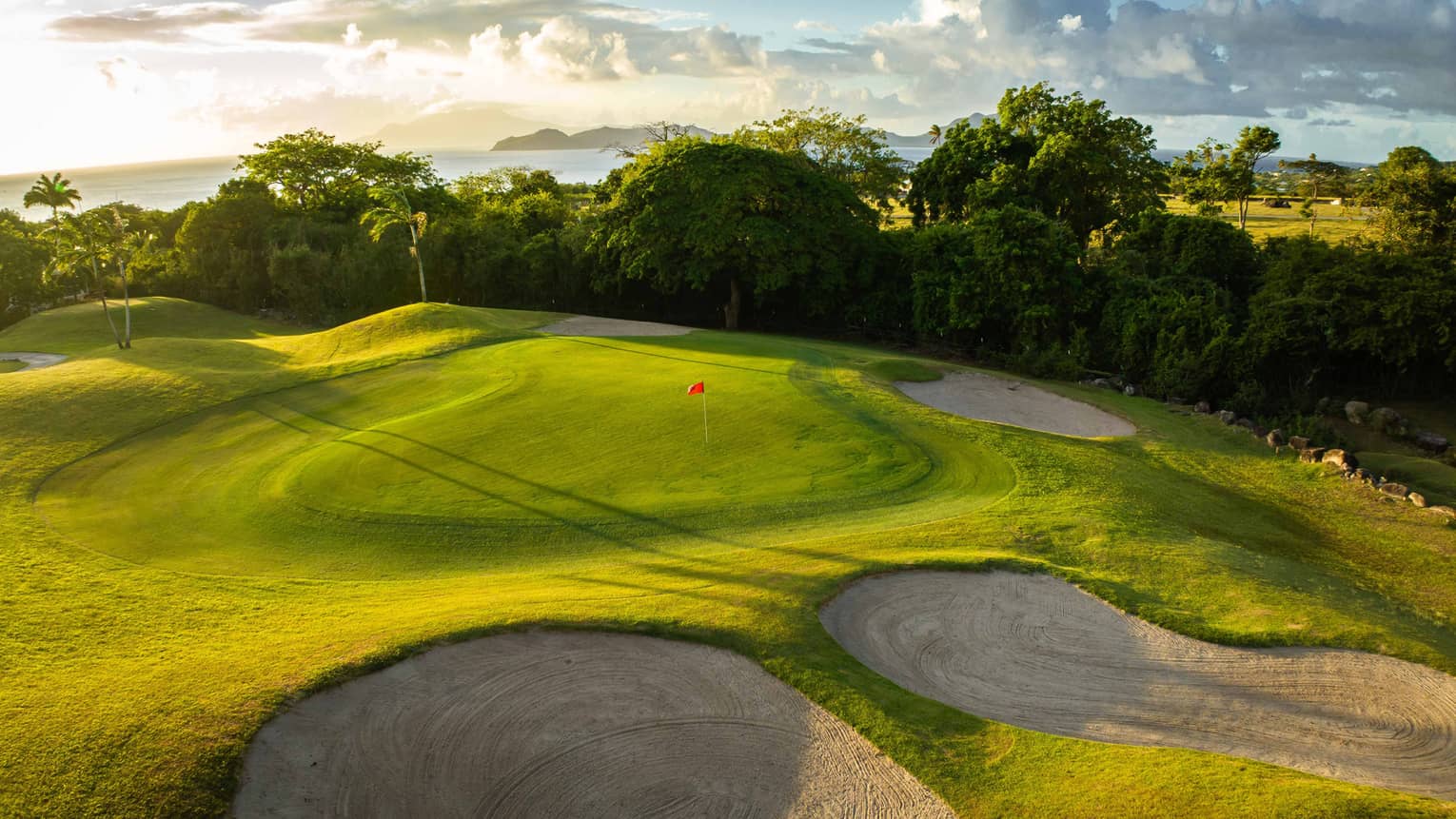 Bird's-eye view of a bright green golf course accented by lush trees and vegetation, under a bright, partly cloudy sky