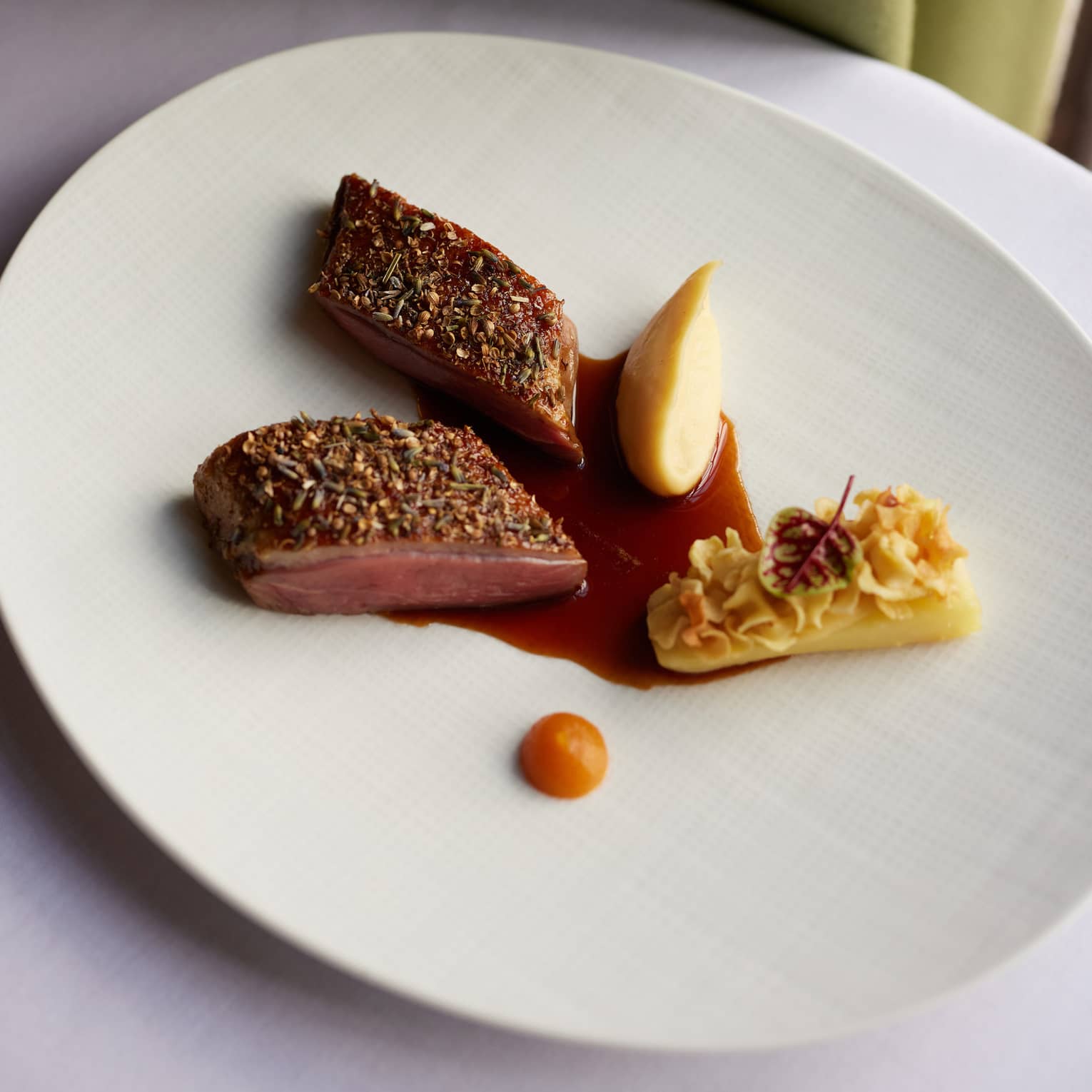 A round white plate holds food items with garnishes and a sauce.