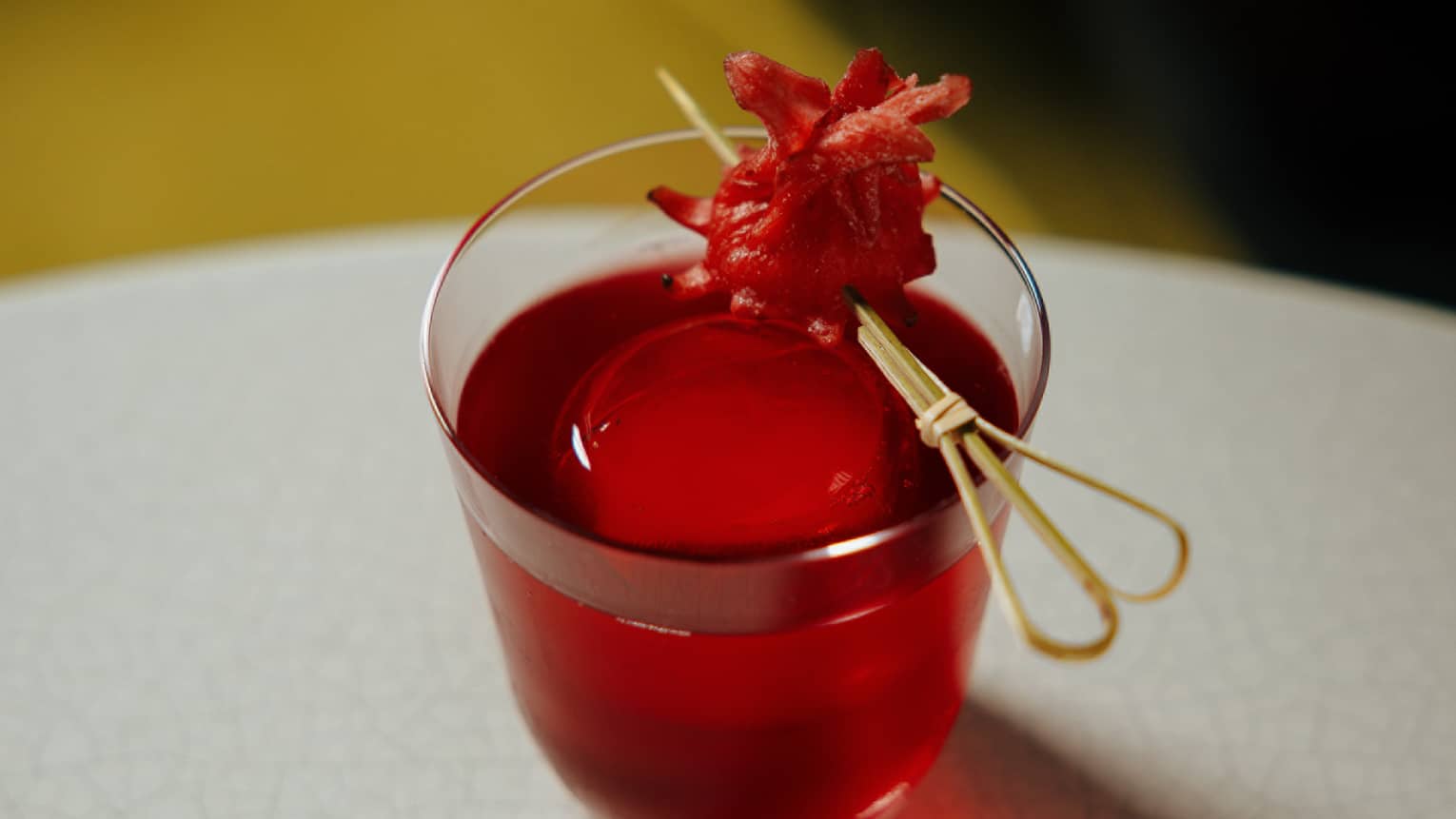 Red-hued cocktail in a rocks glass garnished with a red fruit