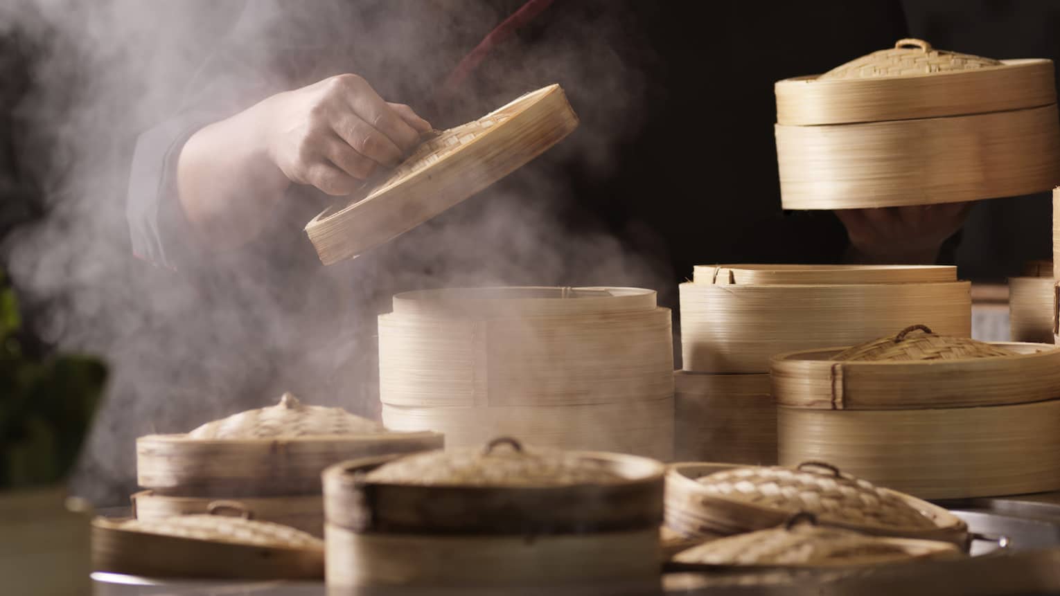 Man lifts top of bamboo steamer, steam rises at Sintoho Dim Sum Station