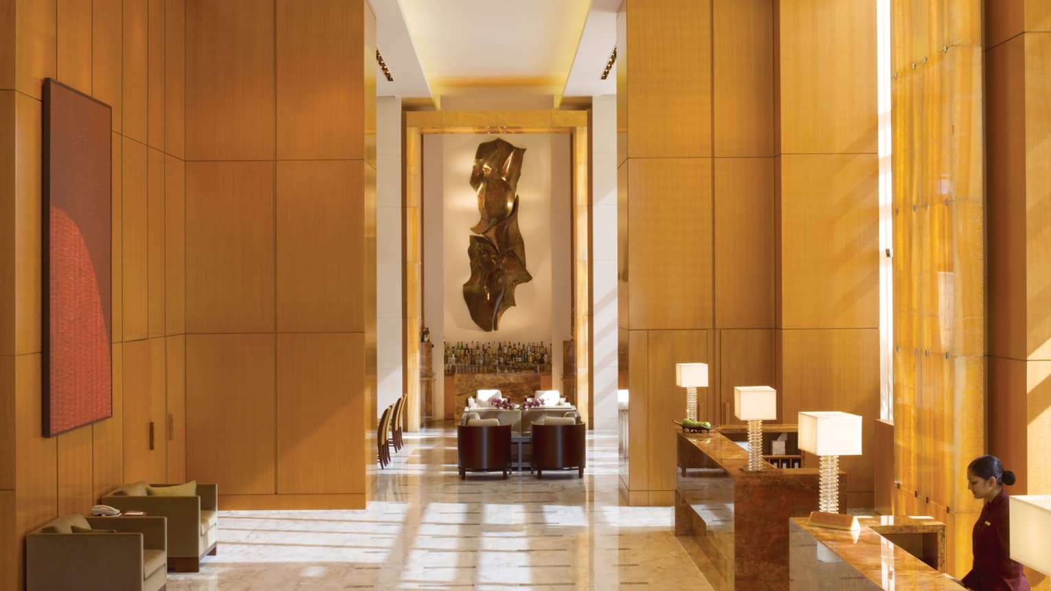 Hotel lobby with soaring ceilings over wood panel walls, marble floors, reception desks