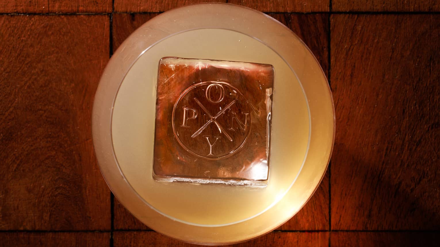 Overhead view of a cocktail with a large ice cube branded with the word "Pony"