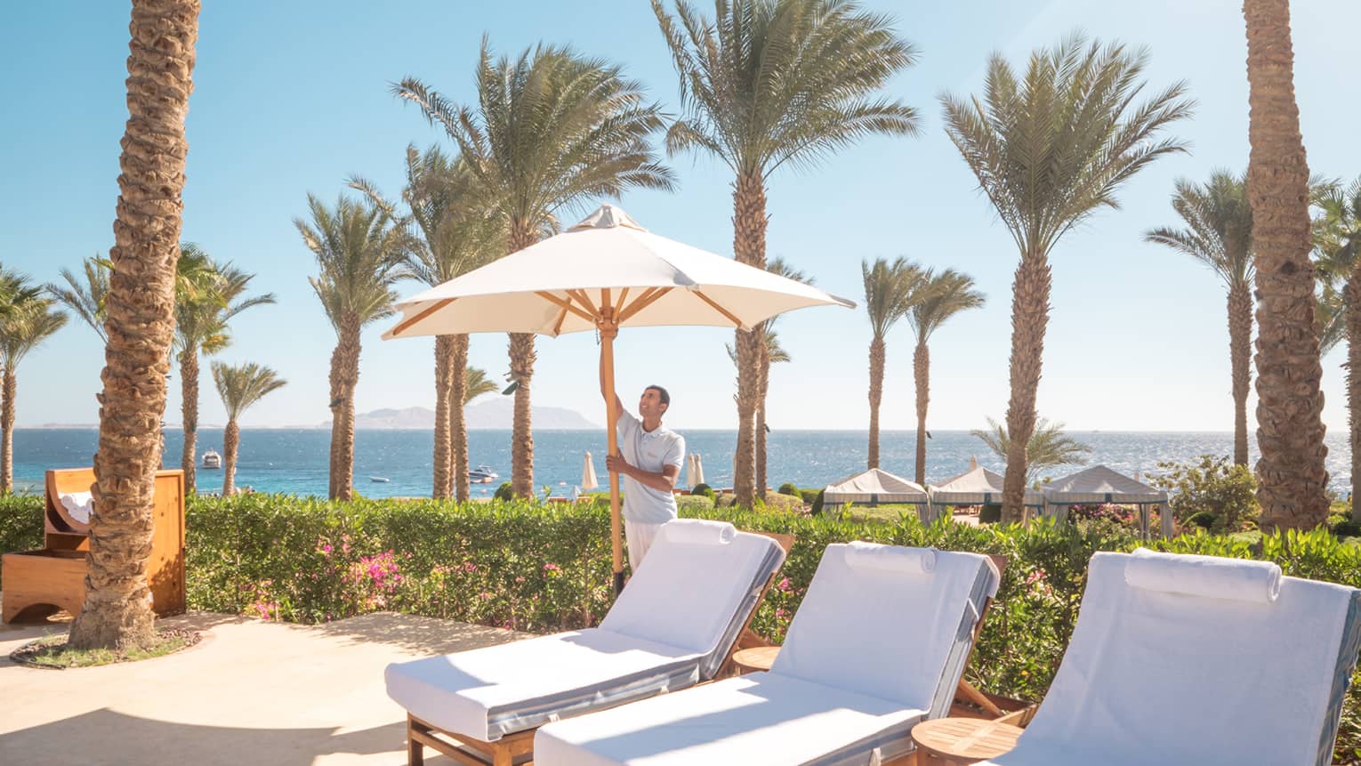 Sun chairs on pool deck, man opening sun umbrella, sea in distance