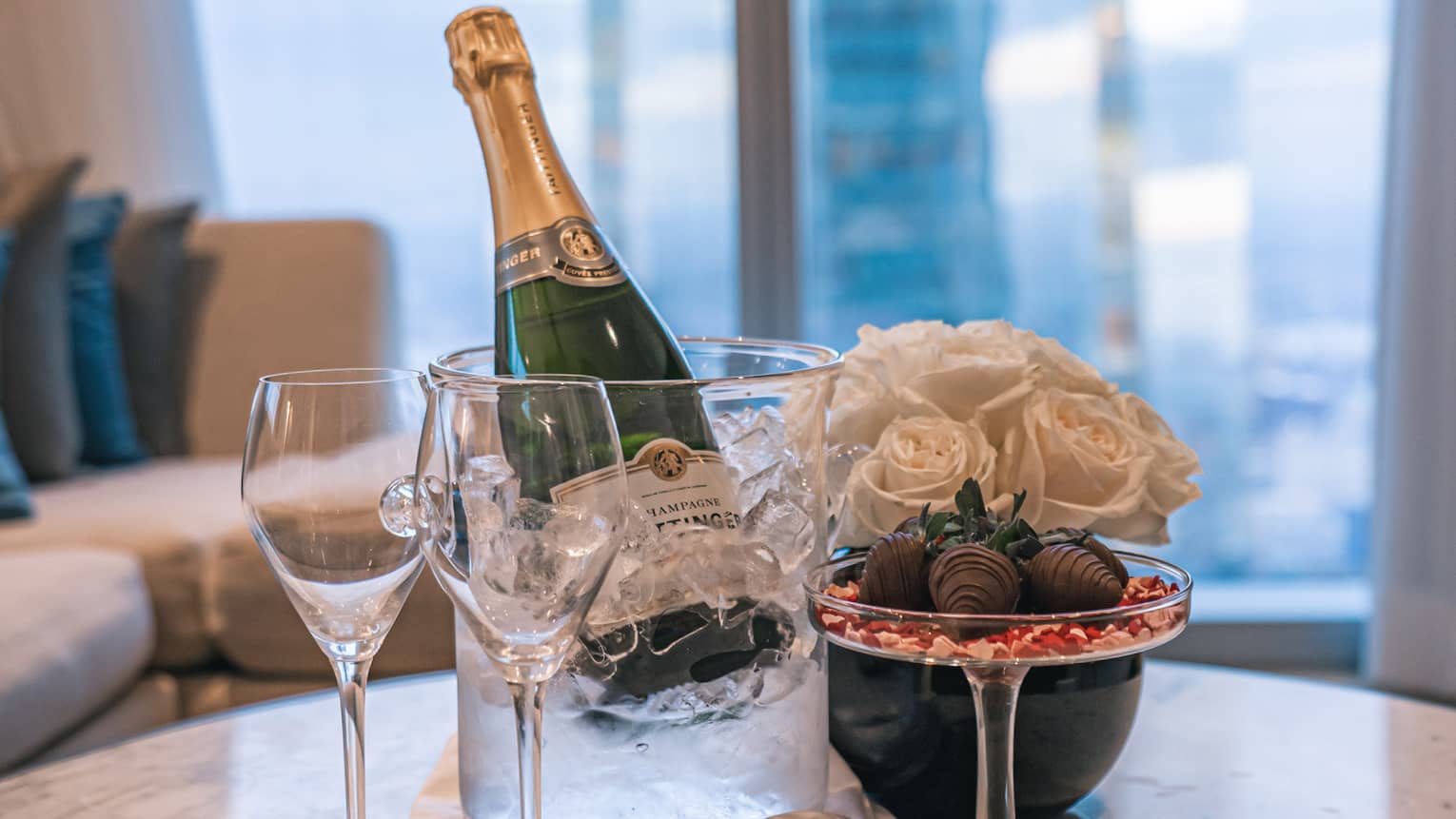 A bottle of Champagne next to a vase of flowers and glasses.