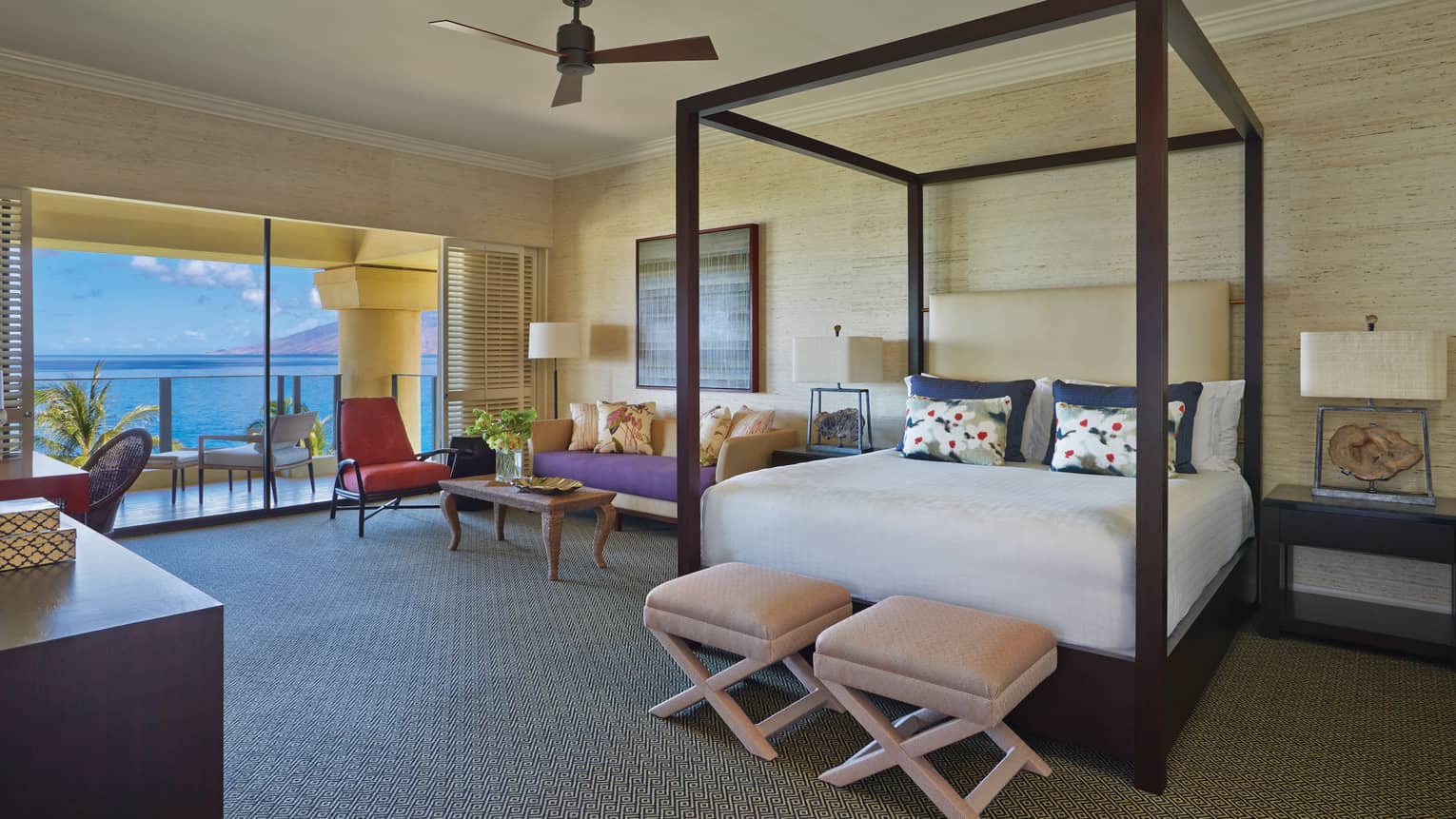 Luxury bedroom with a four-poster bed, seating area and ocean-view balcony at a tropical resort suite