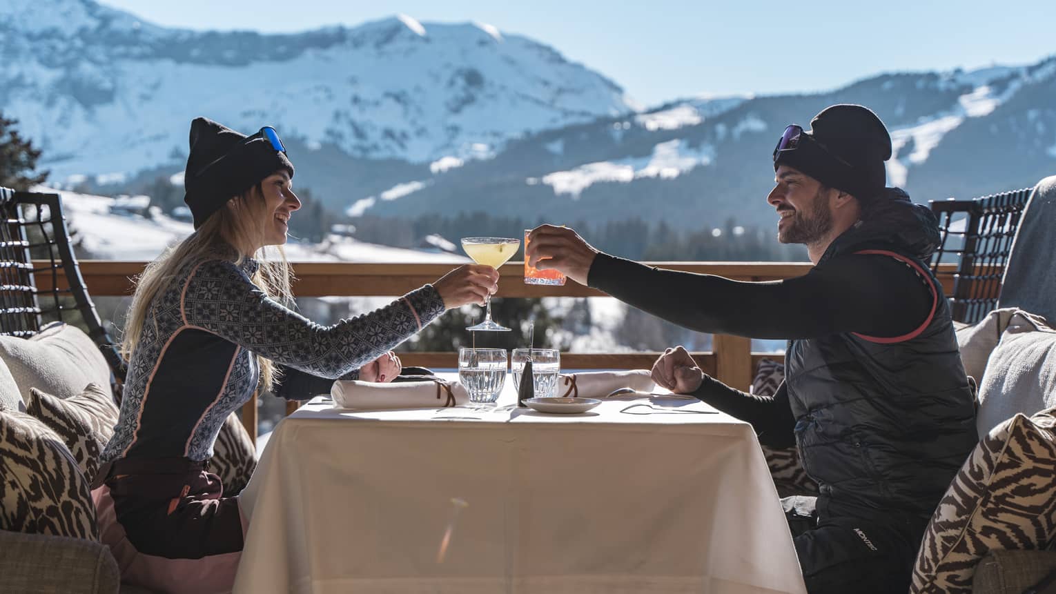 Two people drinking on a patio outside with snowy mountains in the distance