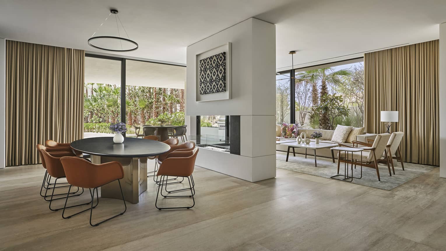 Dining room with oval table and four modern leather chairs, fireplace wall separating living room