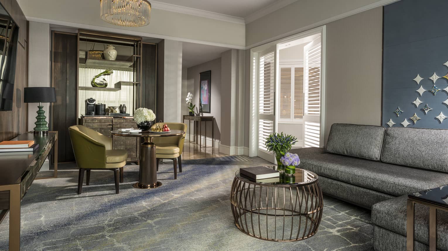Gold dining chairs around small dining table by brass wire table, L-shaped grey sofa