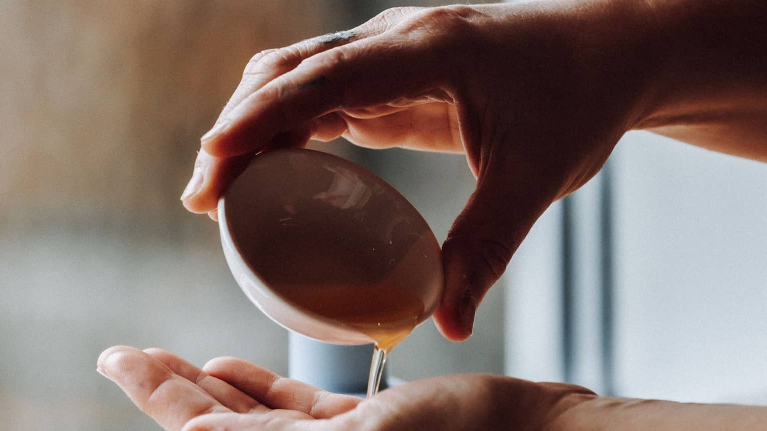 Close-up of a hand pouring liquid into another hand from a small ceramic dish; some other small dishes sit nearby.