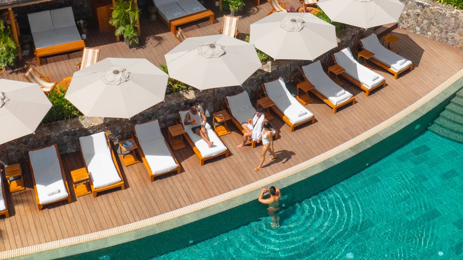 Aerial view of family relaxing on poolside lounge chairs with one person in the water