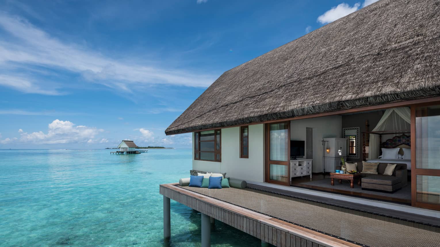 Overwater bungalow with thatched roof, set atop clear turquoise water