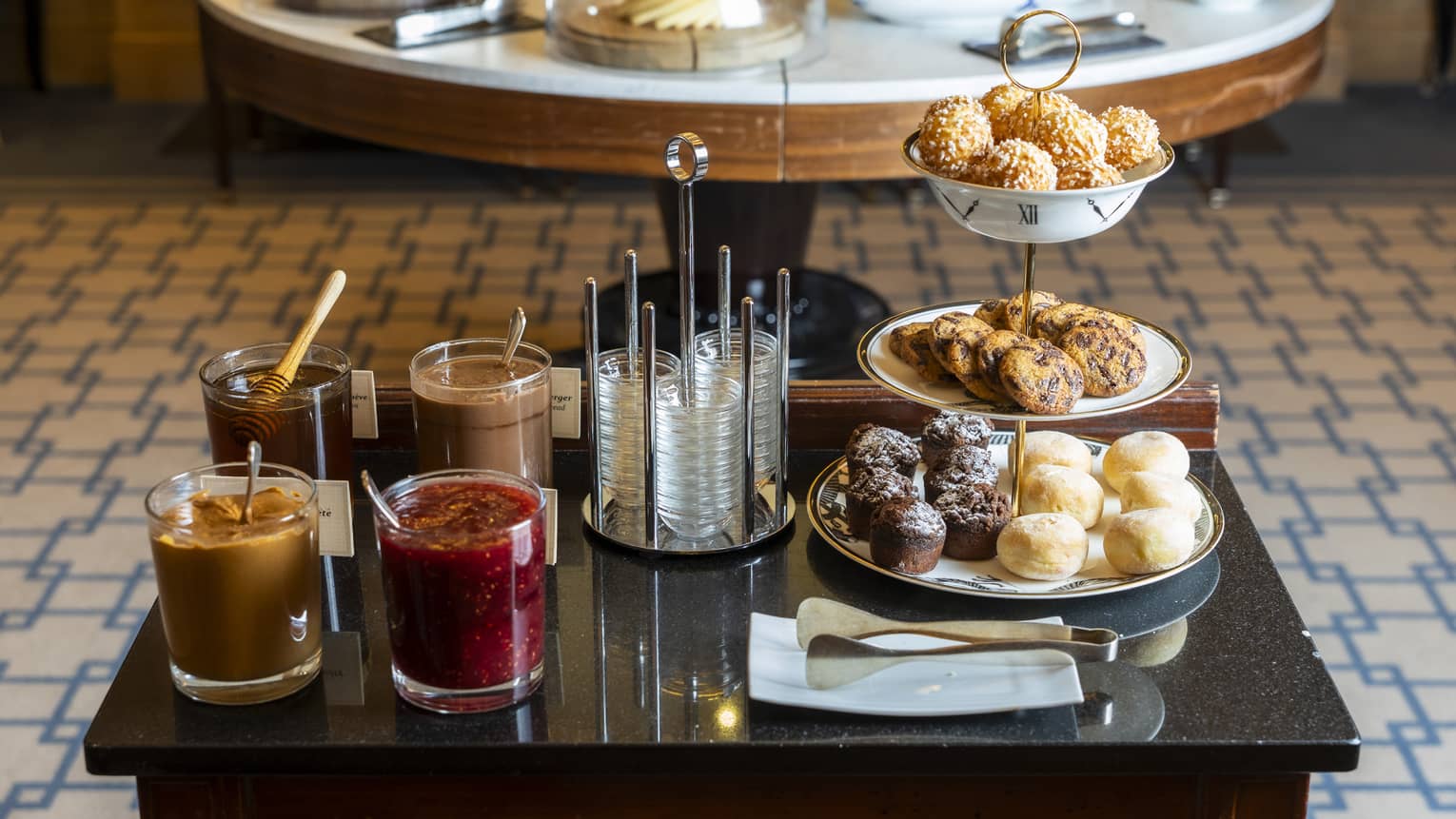 A small table of dark wood holds plates of various breakfast sweets and containers of different spreads.