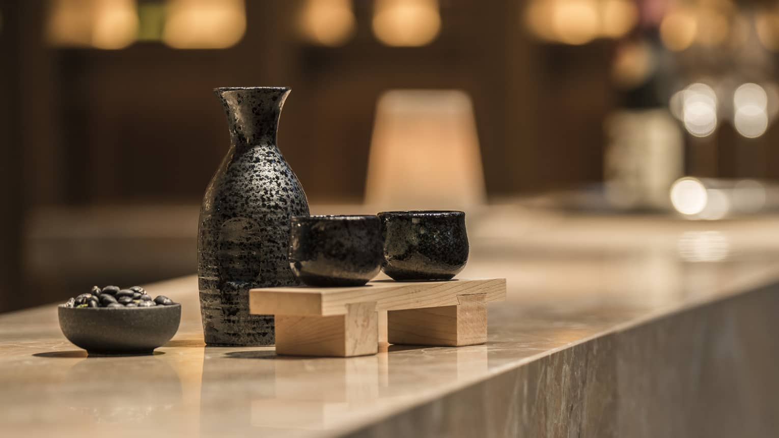 Close-up of black sake jug with two cups on wood tray on marble bar
