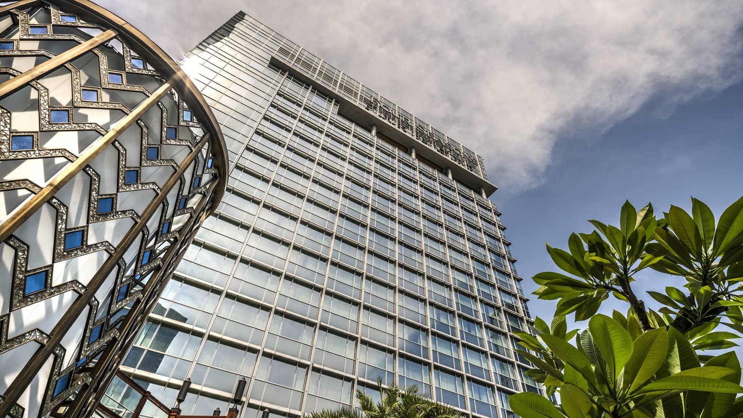 View looking up past tropical plant to glass Four Seasons Hotel Jakarta tower