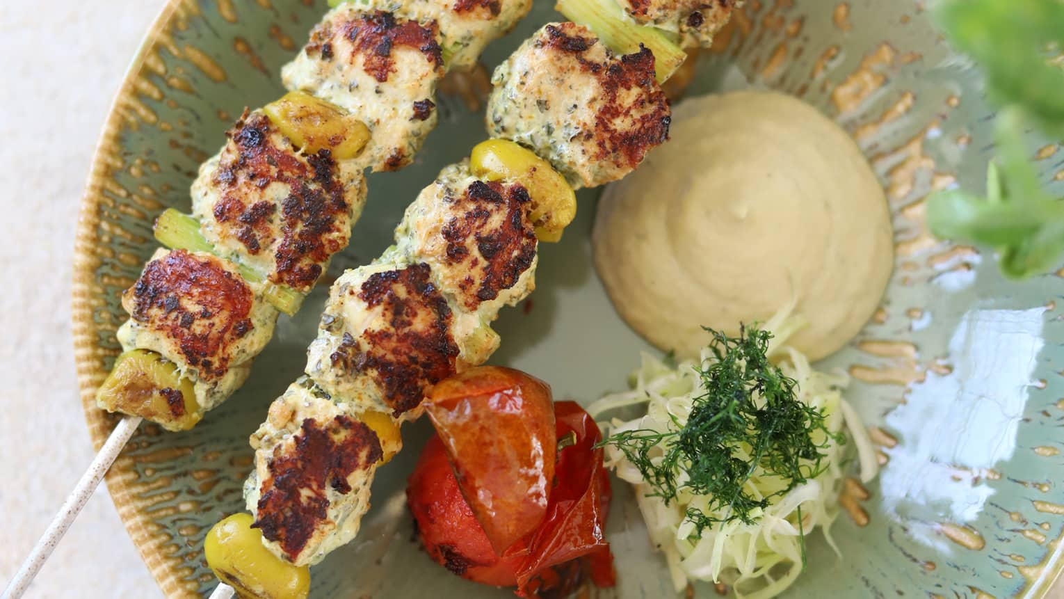 Two Za?atar lemon chicken, olives, roasted fennels and a dollop of garlic dill sauce plated on a sage green round dish