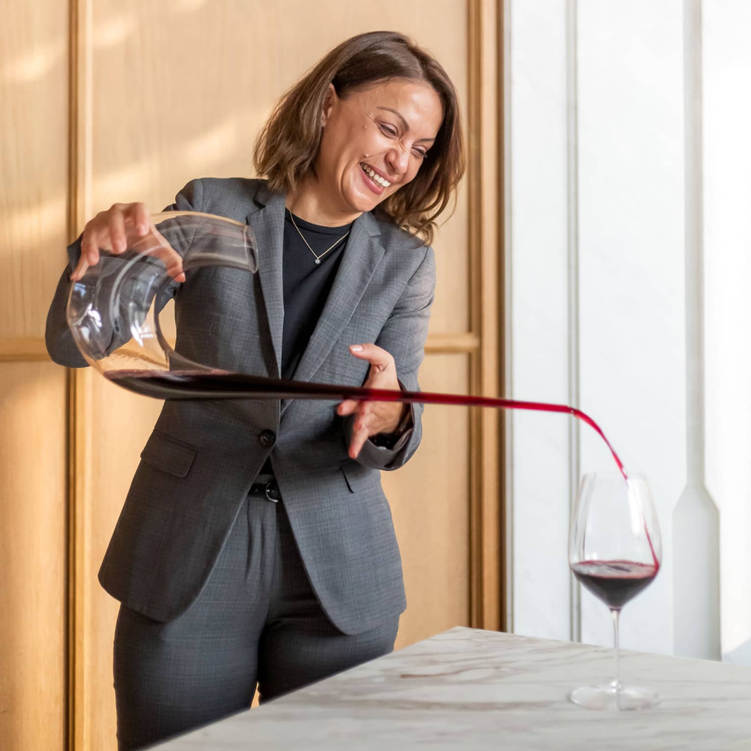 Brasserie Palmier Bar sommelier smiles, pours red wine from long decanter into wine glass on table