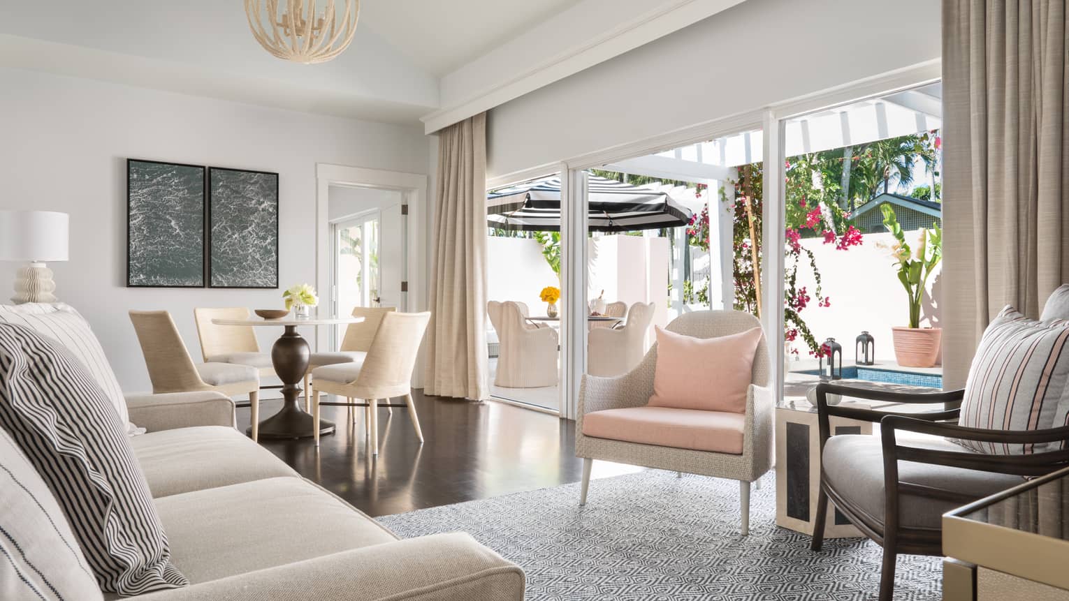Plunge pool living room with neutral tones, featuring a sofa, dining table and sliding doors opening to an outdoor patio with seating and vibrant flowers