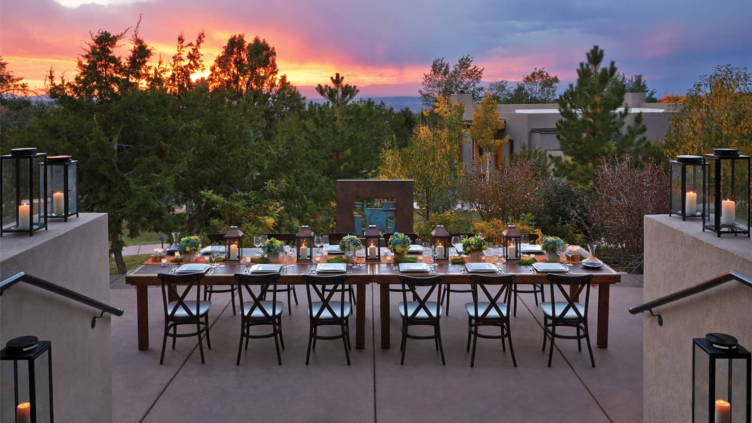 Long, elegant black dining table with black chairs, lanterns and flowers on outdoor terrace at dusk