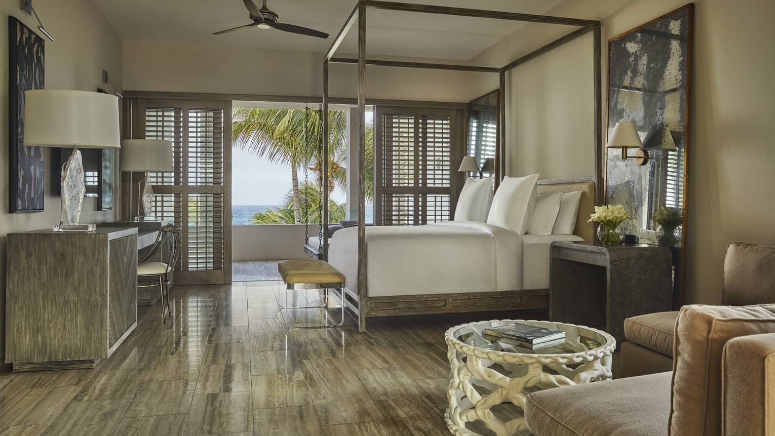 Luxury villa bedroom with a canopy bed, elegant decor, large windows with shutters and a balcony offering ocean and palm tree views