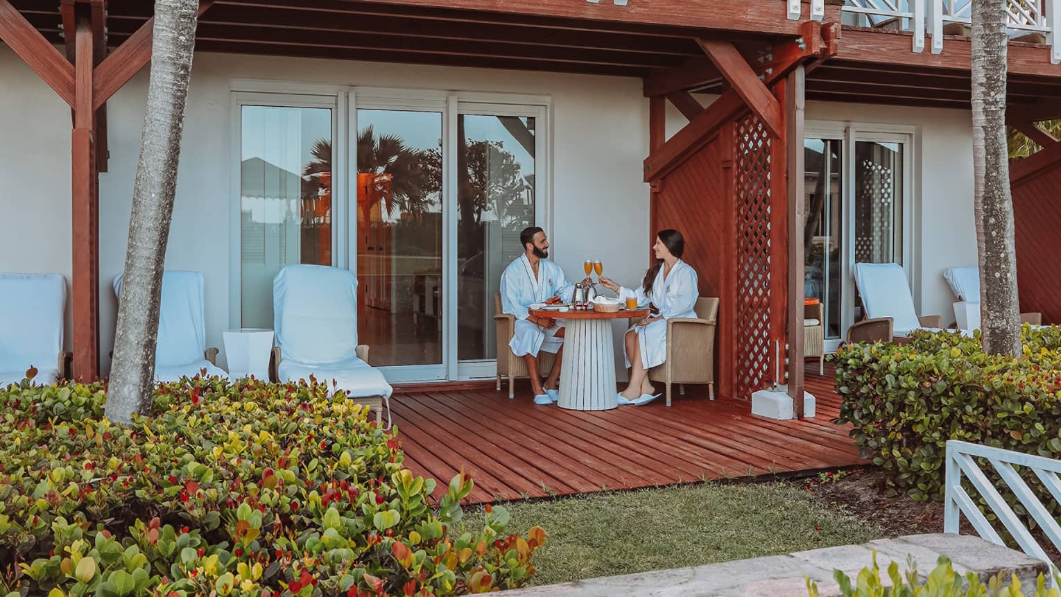 A man and woman sitting outside on a patio surrounded by flowers.