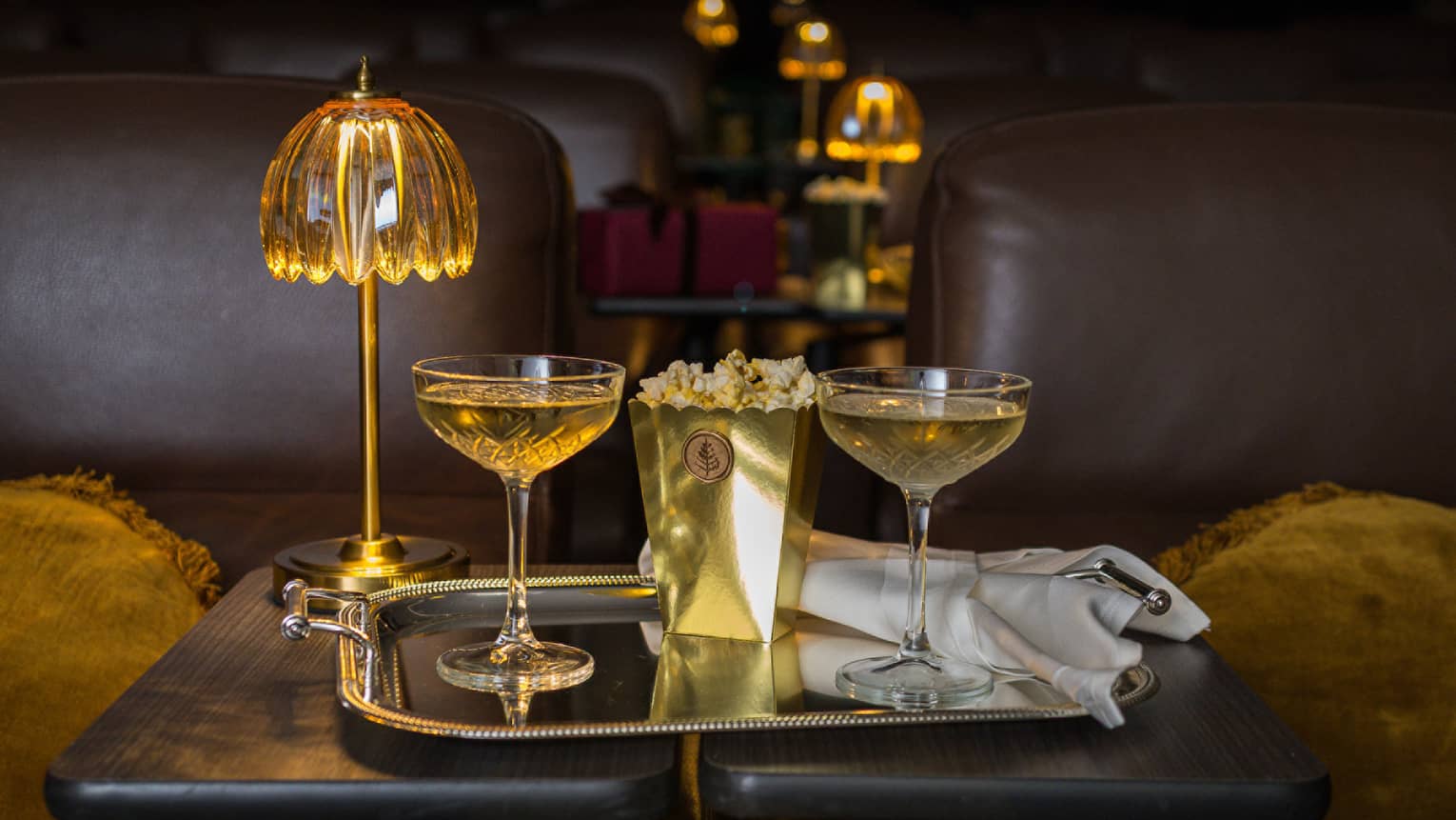 Two filled coupe glasses on a silver serving tray with popcorn in front of a golden dome light.