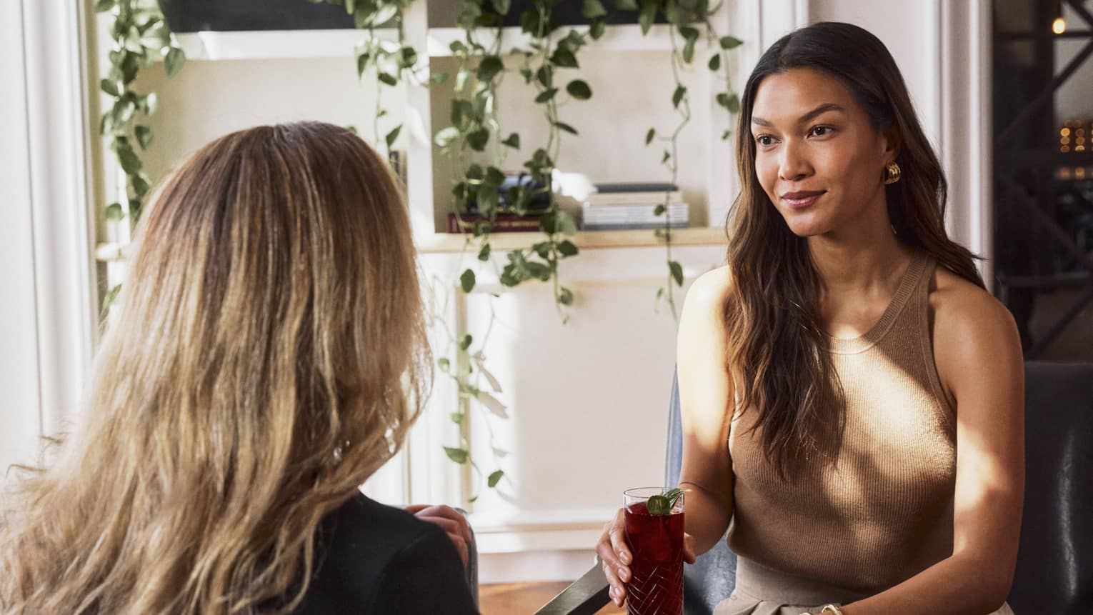 Two guests sitting in chairs facing one another, the wall behind them has four plants.
