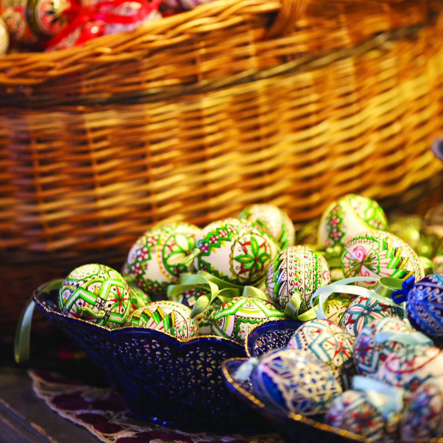 Wicker basketful of red Easter eggs, two small dishes in front with blue and green eggs