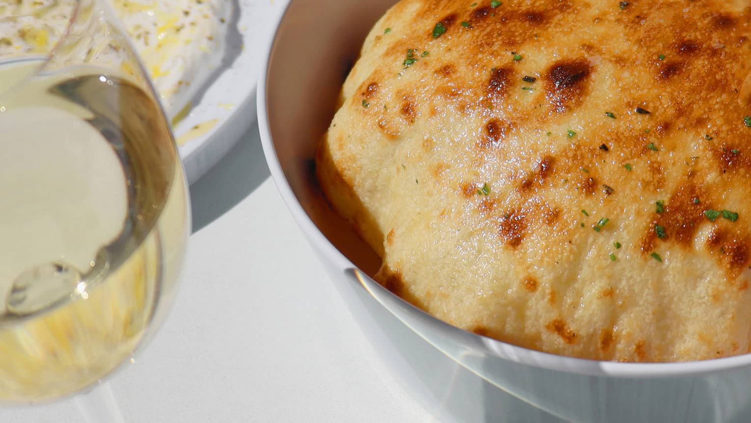 Bread dish in a bowl with a wine glass on the side.