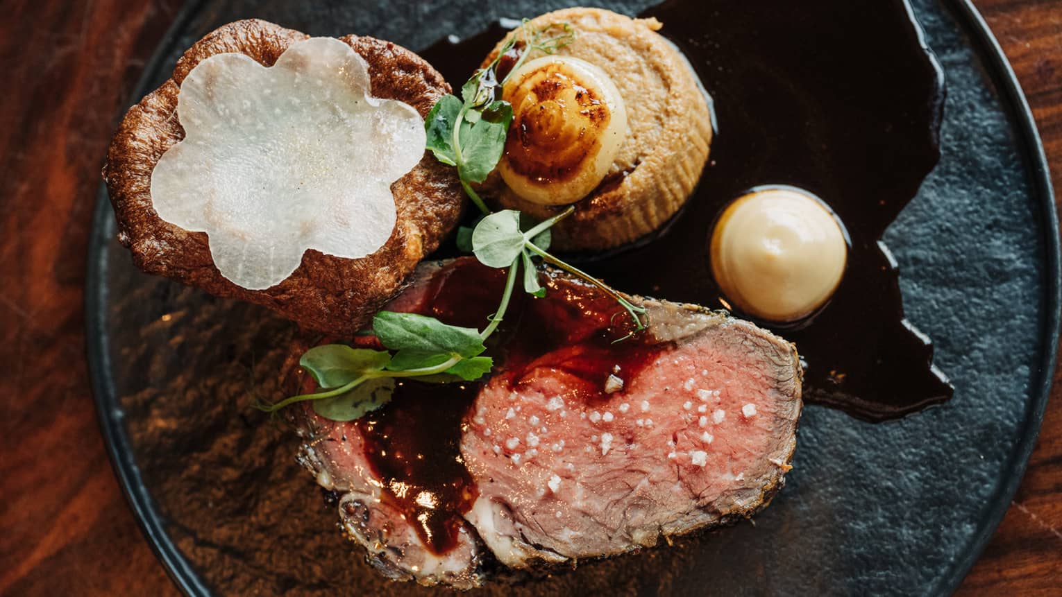 Braised beef short-rib served with caramelized onion and herb souffl� on a round black plate