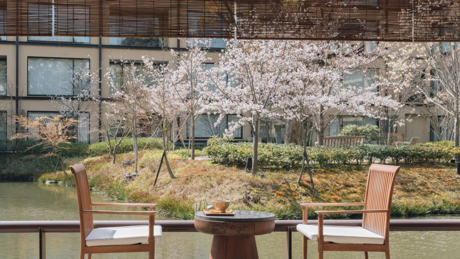 A small round dining table and two chairs on a wooden deck next to pond garden