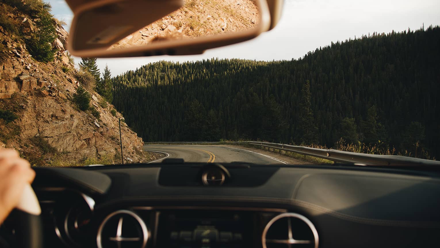 View from behind the wheel of car driving along winding mountain road 