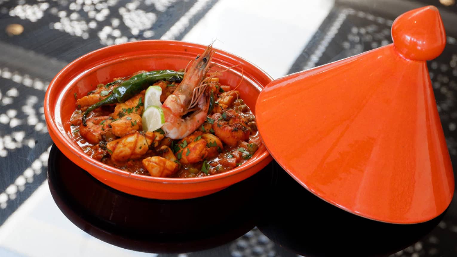 Seafood Tagine fresh fish, prawns in red sauce with lime wedge garnish in red tagine 