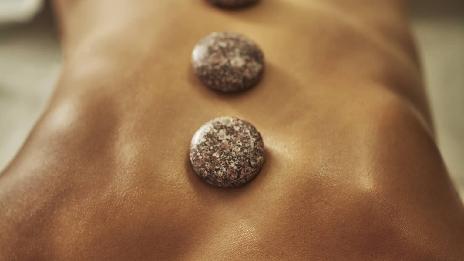 A woman lies on a spa table with four hot stones laid on her back