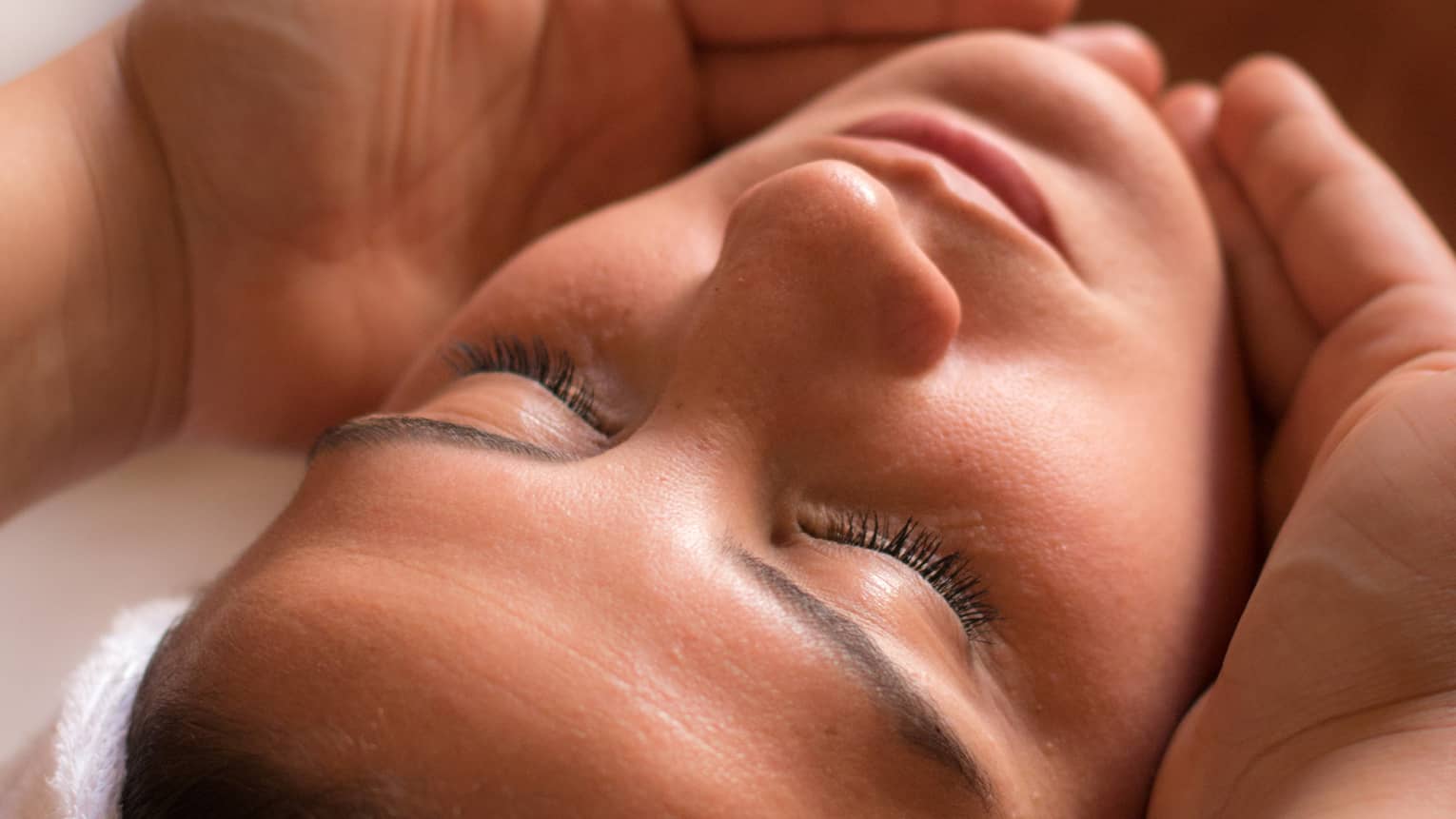 Close-up of woman with eyes closed facing up as hands cup her face and chin