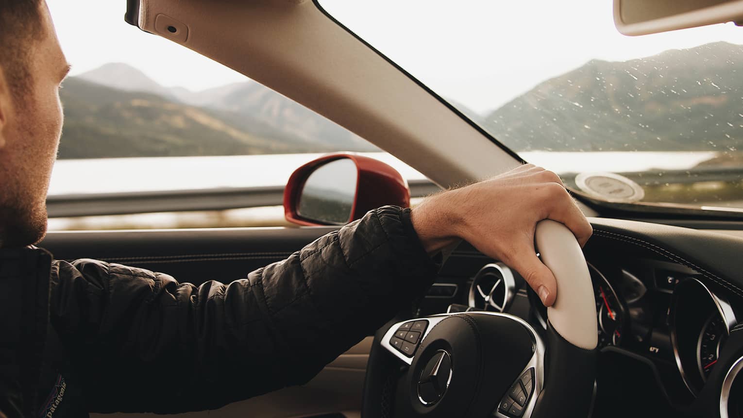 Driver steers wheel of convertible car, mountains in background