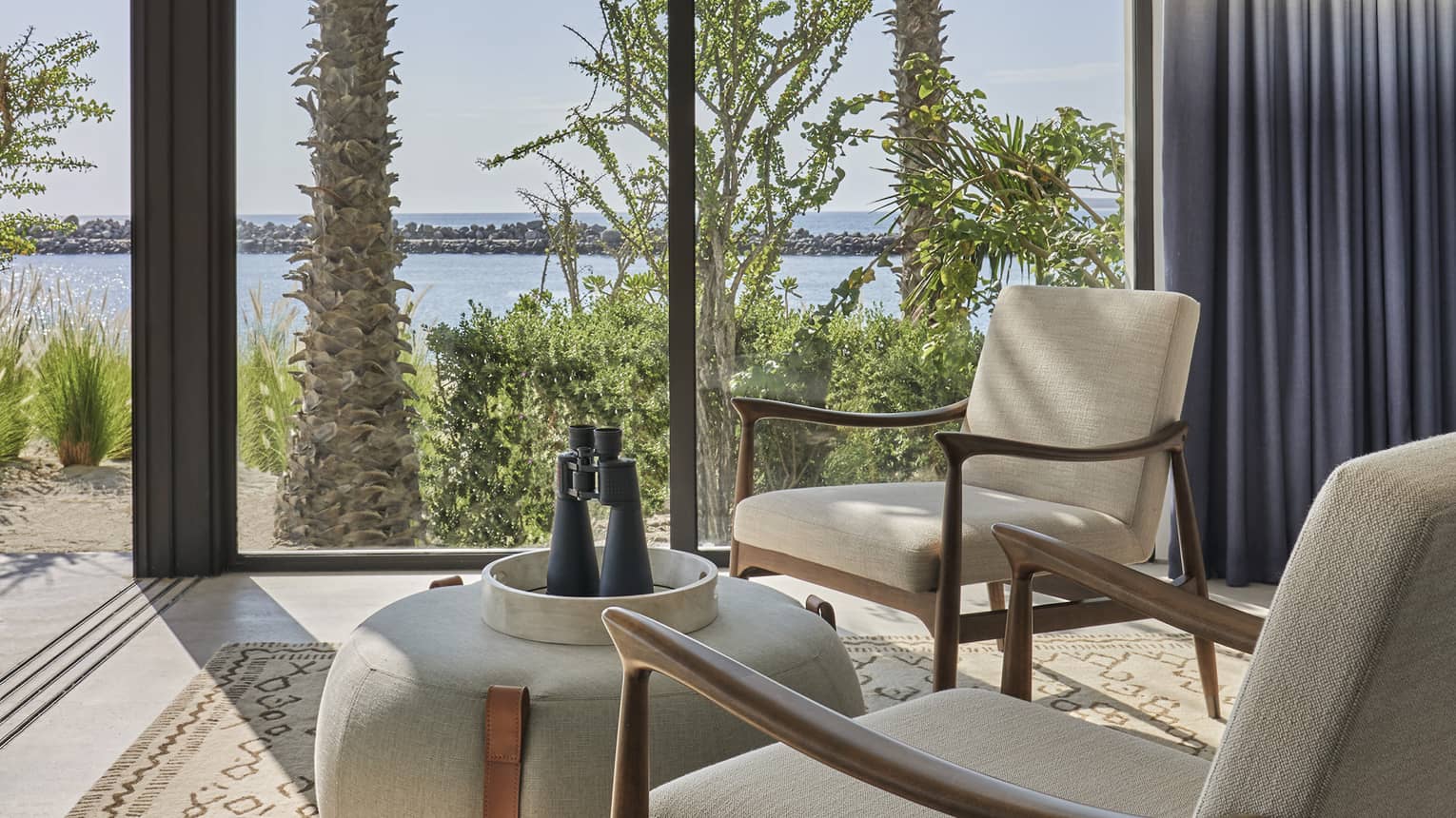 Two Bedroom Sunrise Suite sitting area with twin armchairs, rotund table, floor-to-ceiling windows with ocean views and two-tone curtains